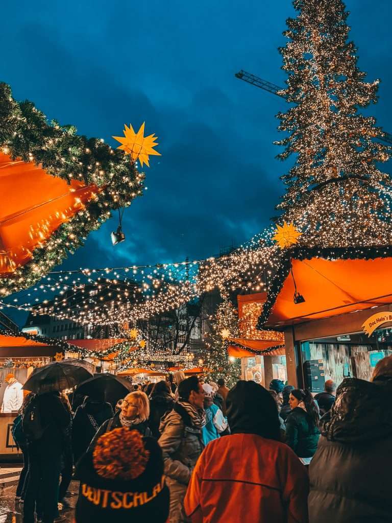Cologne Christmas Markets with charming wooden stalls, twinkling lights, and festive decorations, set against the backdrop of the impressive Cologne Cathedral. Seeds of Travel