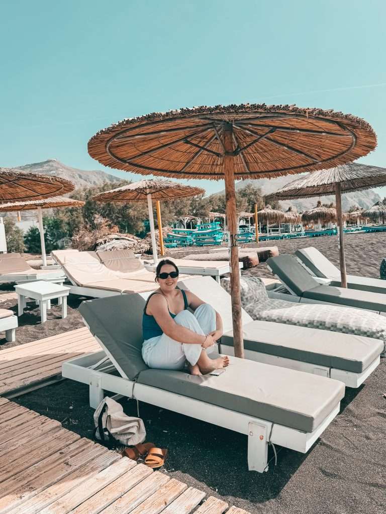 a girl sitting on coralli restaurant beach view in Santorini