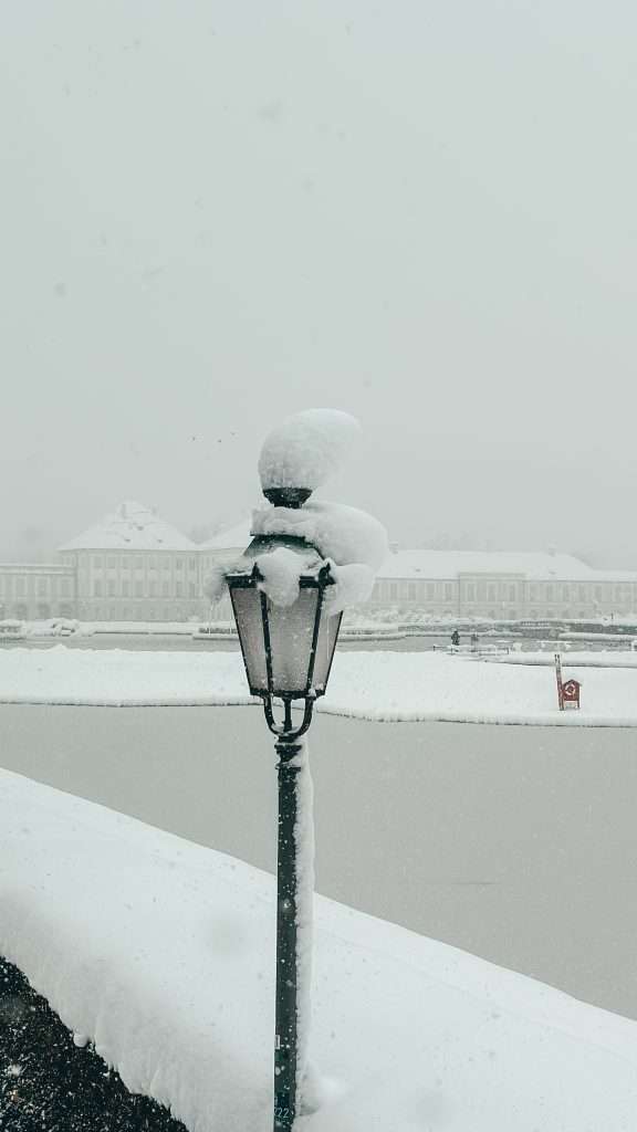 Snow-covered streets and buildings in Munich, with a picturesque winter landscape featuring frosted trees and a serene, white blanket of snow.