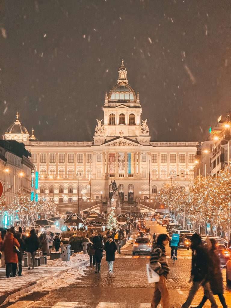 Prague at night during Christmas, illuminated with festive lights and decorations Snow falling Seeds of Travel