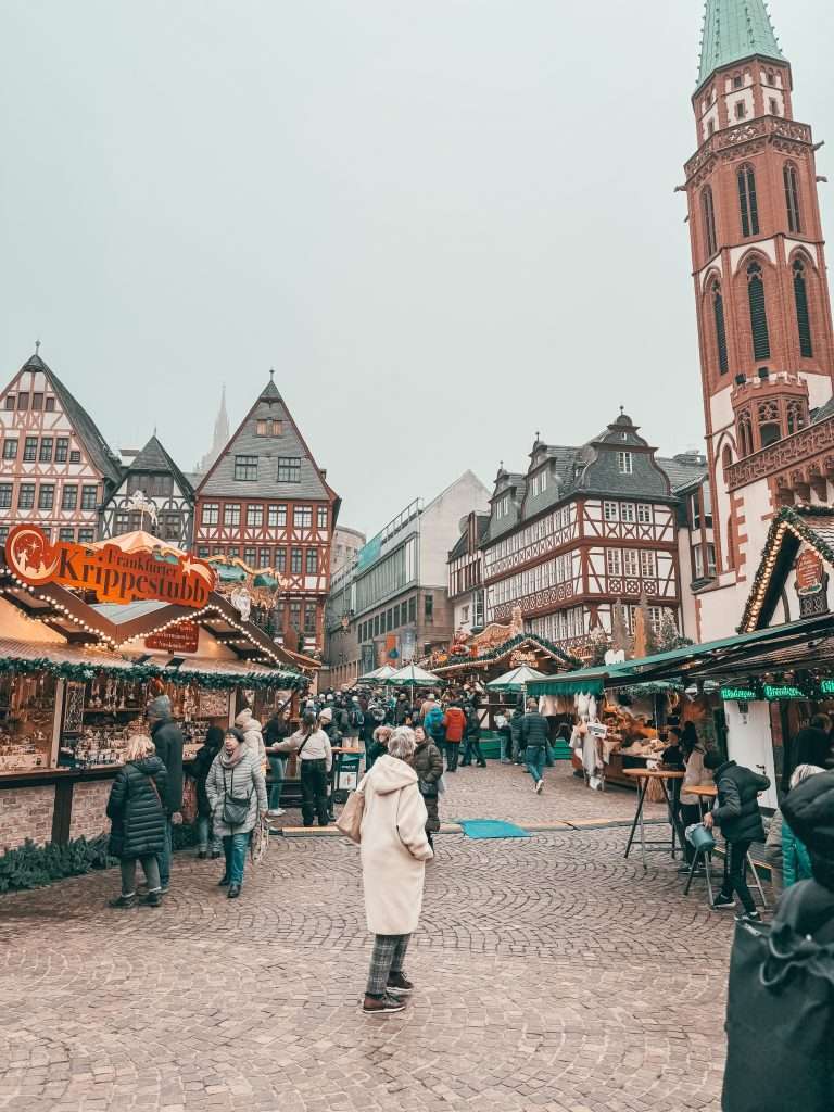Frankfurt Christmas Markets bustling with holiday cheer, featuring traditional wooden stalls, festive lights, and seasonal decorations, with the historic architecture of the city in the background Seeds of Travel