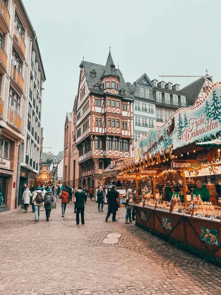 Frankfurt Christmas Markets bustling with holiday cheer, featuring traditional wooden stalls, festive lights, and seasonal decorations, with the historic architecture of the city in the background Seeds of Travel
